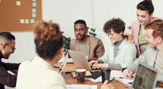 A meeting of young, diverse people sitting around a wooden table with laptops