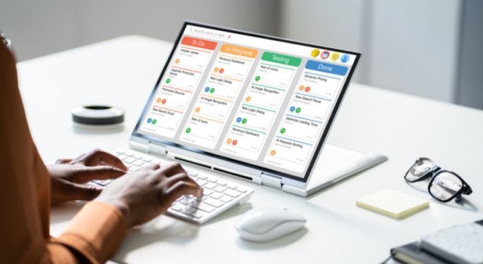 A project manager with a screen showing a kanban board of tasks: to do, in progress, testing, and done.