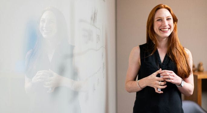 A smiling woman presenting in front of a whiteboard.