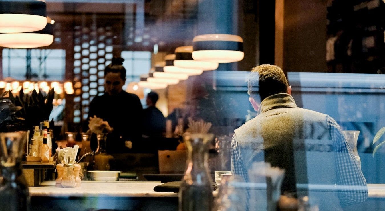 A gentleman stands confidently in front of a well-lit bar, exuding an air of sophistication and anticipation.