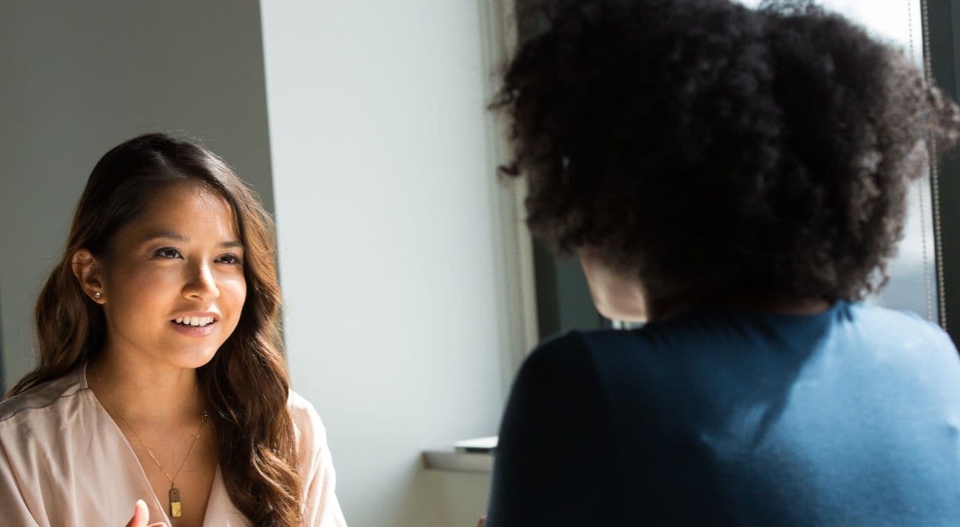 Two women engaged in conversation inside an office setting.