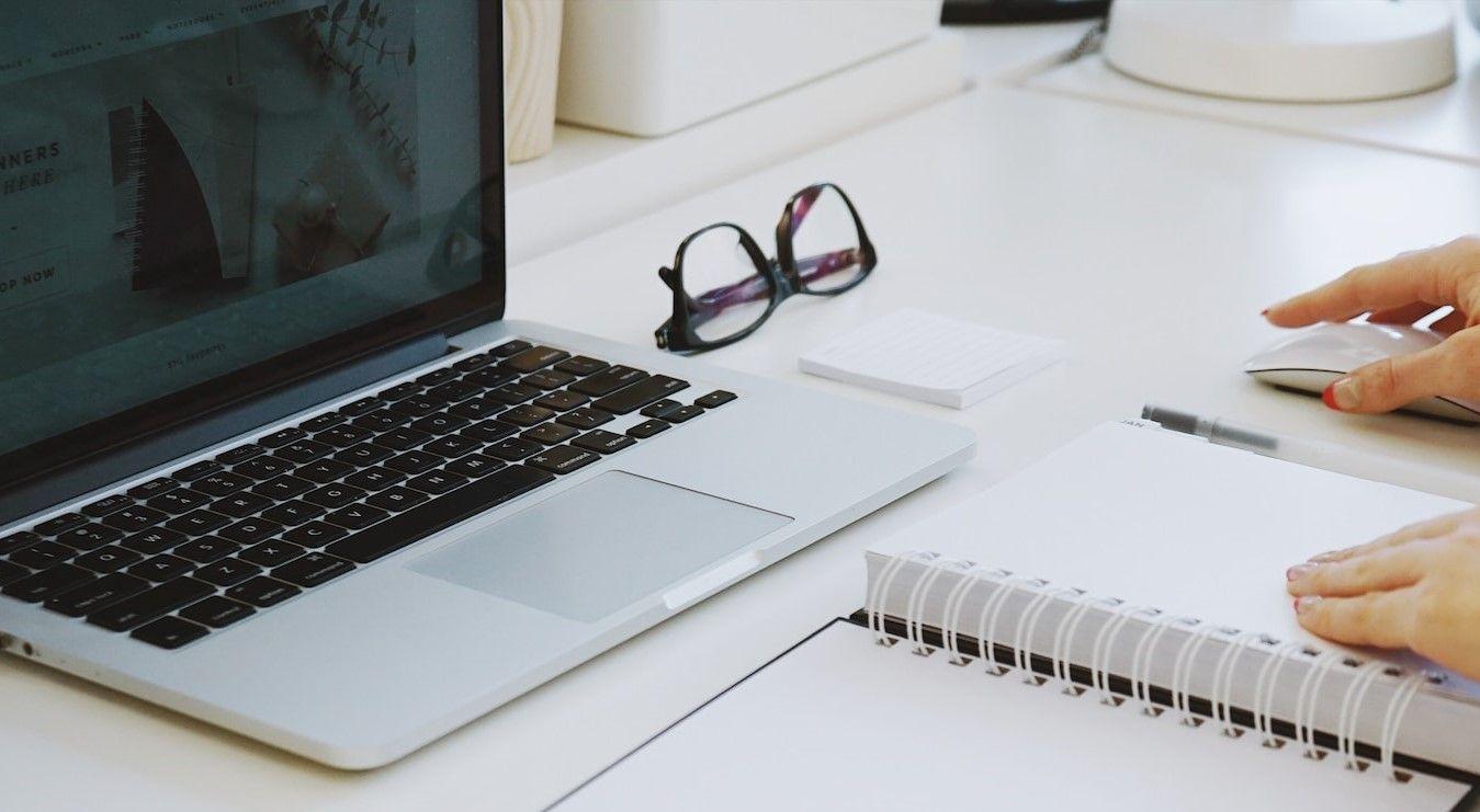 A person diligently typing on a laptop while simultaneously jotting down notes in a notebook.