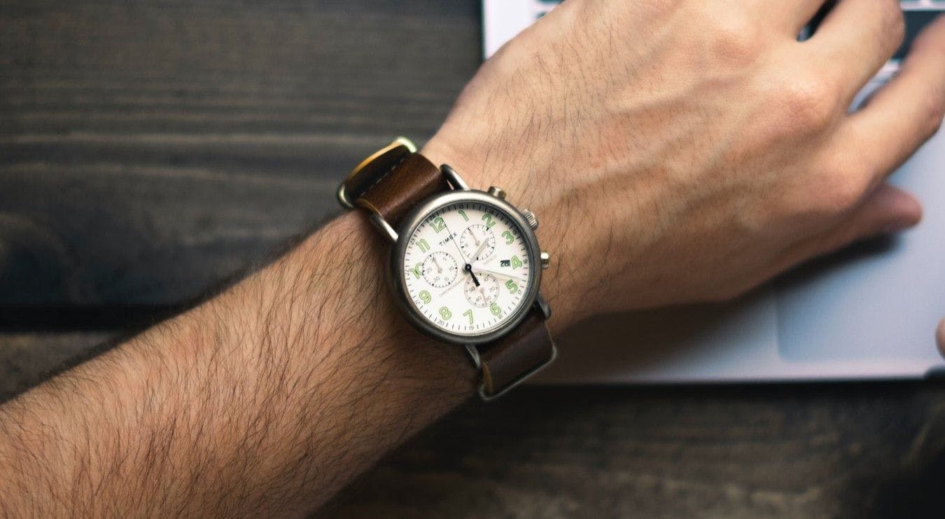  A person wearing a wristwatch sits beside a laptop, ready to work or keep track of time.