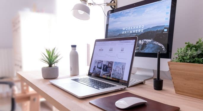 An at-home work setup for a digital marketer, features several plants, a macbook, monitor, desk light and mouse.